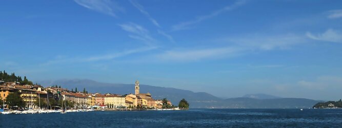 GranCanariaFerienwohnung beliebte Urlaubsziele am Gardasee -  Mit einer Fläche von 370 km² ist der Gardasee der größte See Italiens. Es liegt am Fuße der Alpen und erstreckt sich über drei Staaten: Lombardei, Venetien und Trentino. Die maximale Tiefe des Sees beträgt 346 m, er hat eine längliche Form und sein nördliches Ende ist sehr schmal. Dort ist der See von den Bergen der Gruppo di Baldo umgeben. Du trittst aus deinem gemütlichen Hotelzimmer und es begrüßt dich die warme italienische Sonne. Du blickst auf den atemberaubenden Gardasee, der in zahlreichen Blautönen schimmert - von tiefem Dunkelblau bis zu funkelndem Türkis. Majestätische Berge umgeben dich, während die Brise sanft deine Haut streichelt und der Duft von blühenden Zitronenbäumen deine Nase kitzelt. Du schlenderst die malerischen, engen Gassen entlang, vorbei an farbenfrohen, blumengeschmückten Häusern. Vereinzelt unterbricht das fröhliche Lachen der Einheimischen die friedvolle Stille. Du fühlst dich wie in einem Traum, der nicht enden will. Jeder Schritt führt dich zu neuen Entdeckungen und Abenteuern. Du probierst die köstliche italienische Küche mit ihren frischen Zutaten und verführerischen Aromen. Die Sonne geht langsam unter und taucht den Himmel in ein leuchtendes Orange-rot - ein spektakulärer Anblick.